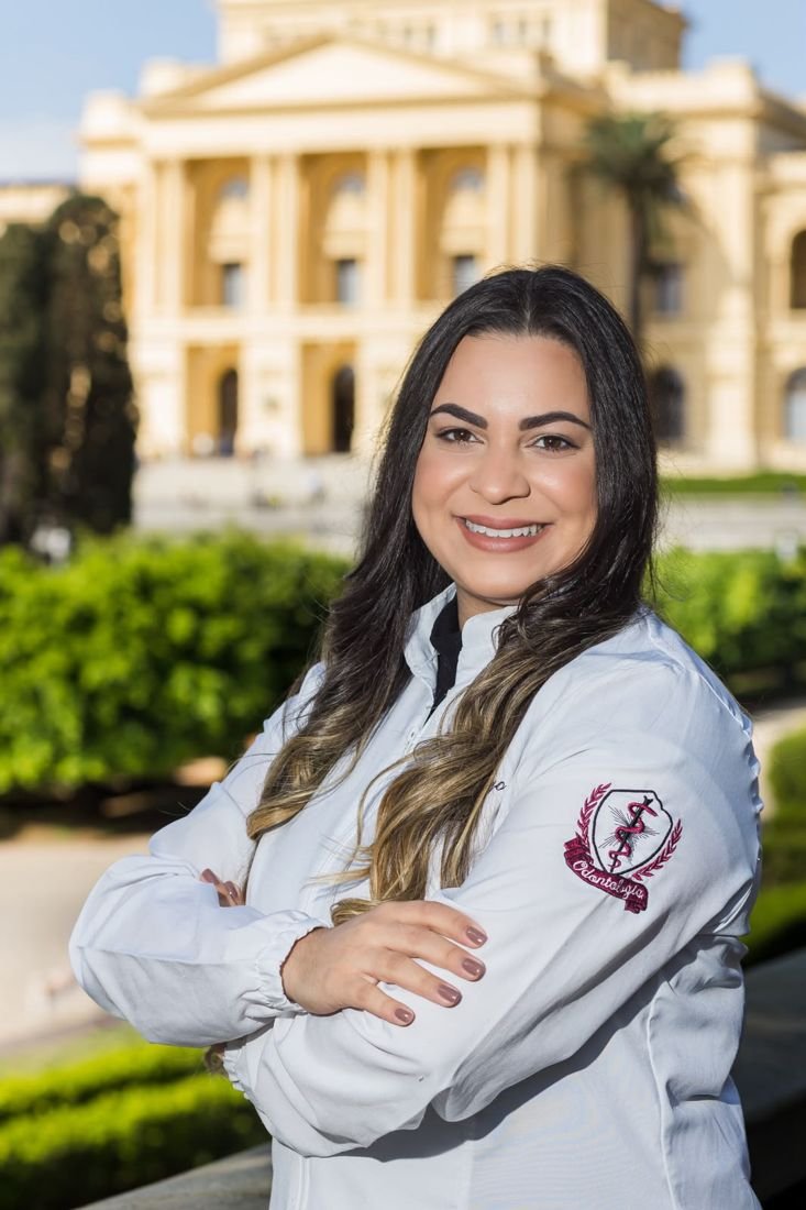 Dra. Kamila Carazzatto de jaleco branco com o brasão da Odontologia.